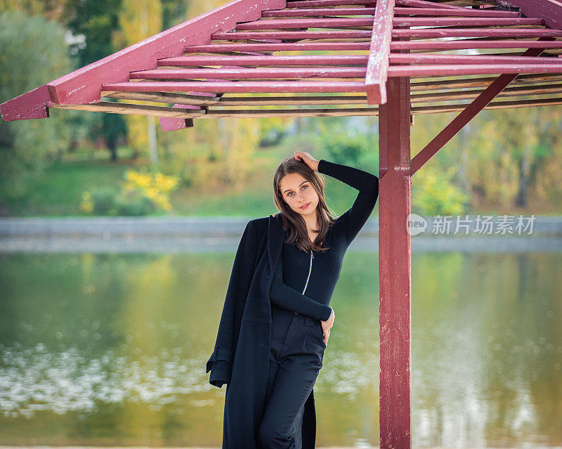 一个美丽的女孩在秋天的公园里撑着伞站在池塘边。