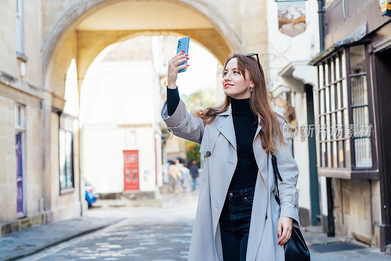 年轻的女游客参观一个风景如画的城市街道目的地，在假期和旅行期间用智能手机拍照，在古老的欧洲城市，户外散步。游览市区