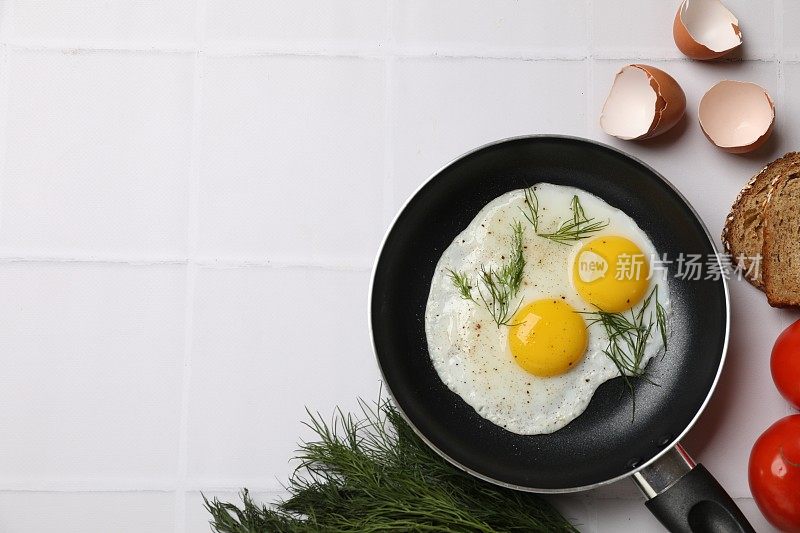 用煎锅将美味的煮熟的鸡蛋、莳萝等产品放在白色的瓷砖桌上，平铺。文本空间