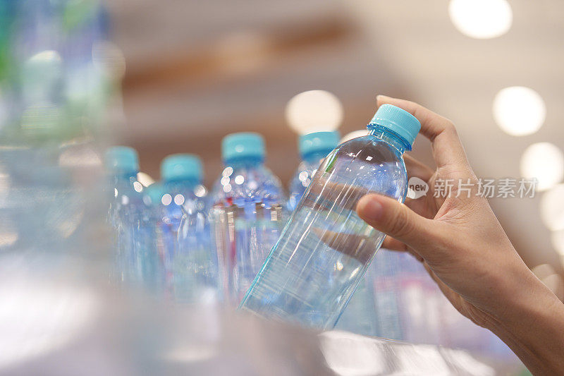 特写女人的手，一个女人从杂货店的架子上挑选一瓶水