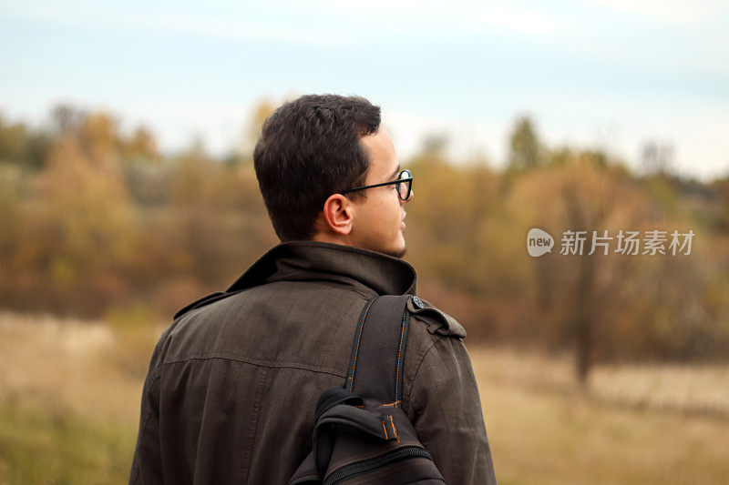 后视图游客冒险男子与背包站在秋天的自然背景。人类喜欢鼓舞人心的史诗景观。模糊