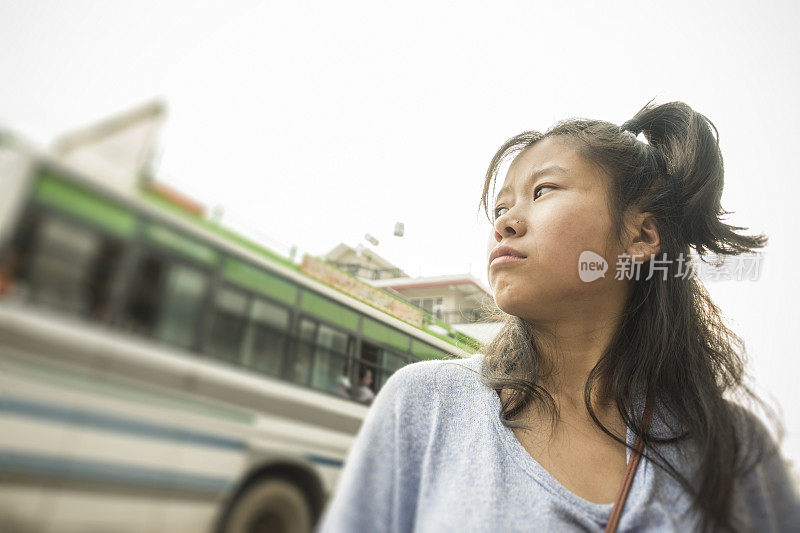 一个亚洲女孩在路边等公车。