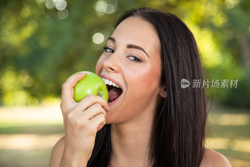 美丽的年轻女子在户外拿着咬人的新鲜苹果