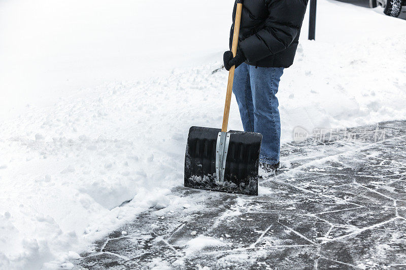 穿冬季夹克的人正在铲人行道上的雪