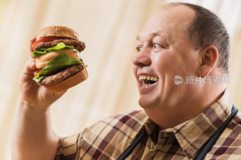 一个超重的兴奋的男人要吃一个巨大的汉堡。