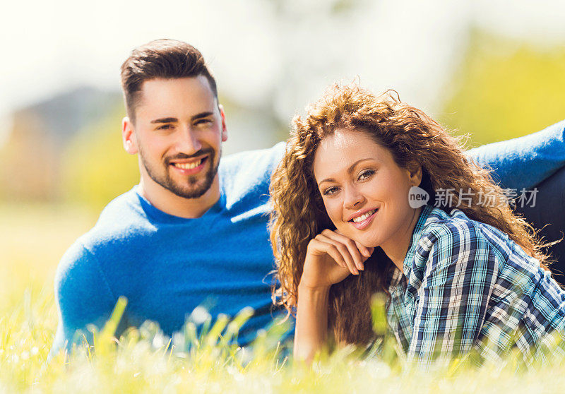 一对微笑的情侣在草地上放松，看着镜头。
