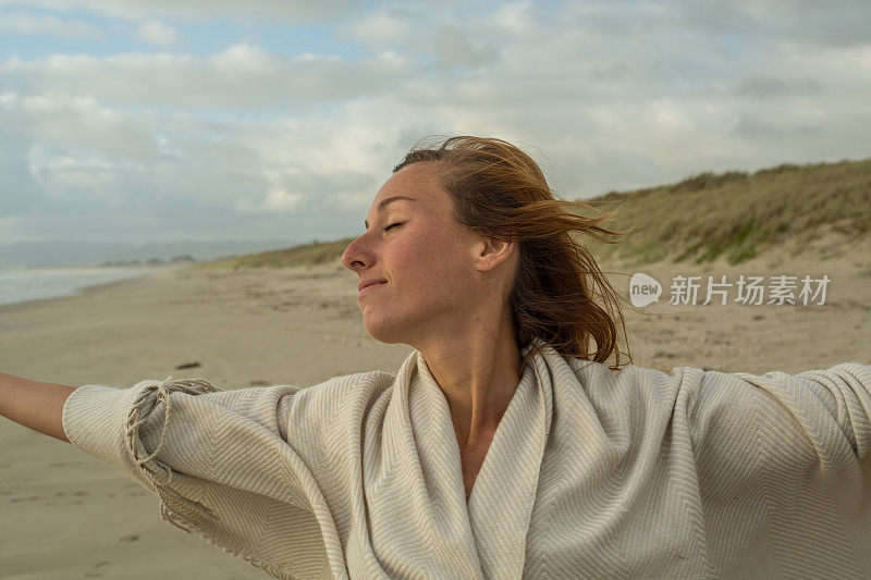 日落时分，快乐的年轻女子在海滩上张开双臂