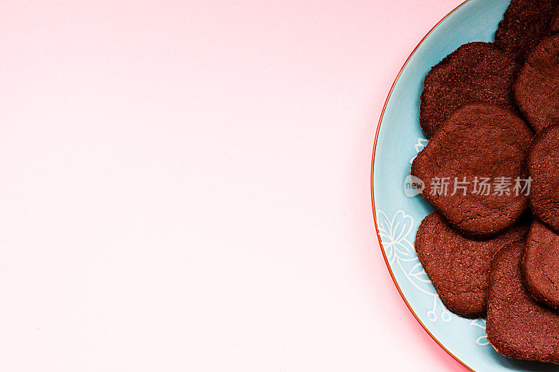 蓝色盘子里的巧克力饼干，粉红色的背景。前视图。平的。现代食品的概念。