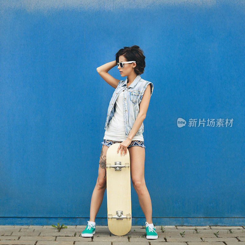 年轻的黑发女子与滑板摆姿势