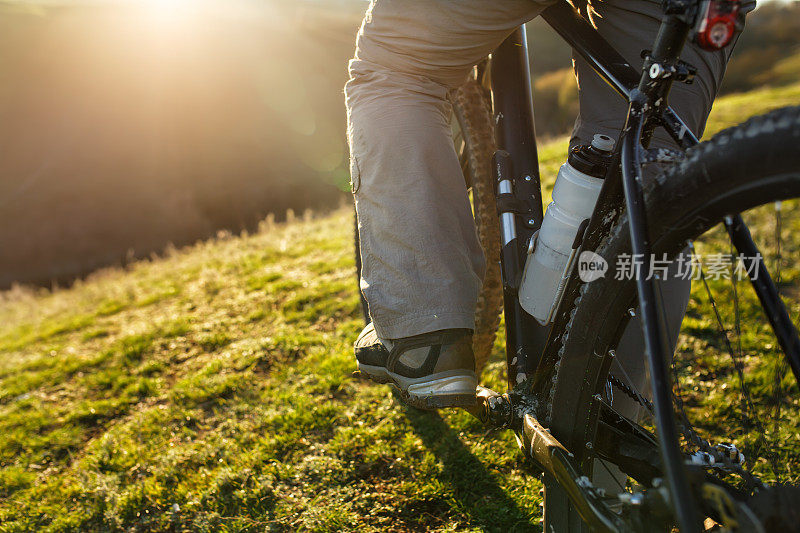 特写的人的腿骑山地车在户外小径在绿色的田野。