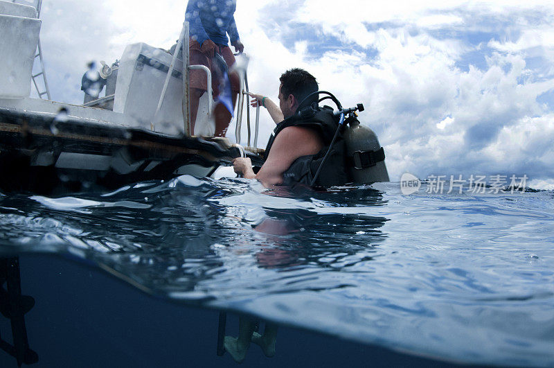 在船后面的男性潜水员取下鱼鳍回到船的水上和水下摄像机爬上梯子