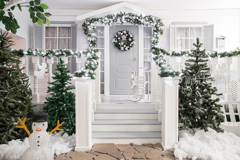 房屋入口为节日装饰。圣诞装饰。栏杆上用冷杉树枝编成的花环和灯