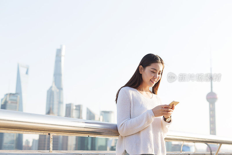 年轻美丽的亚洲女人在现代城市玩手机