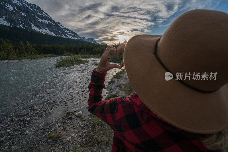 年轻女子在山景上做心形手指架