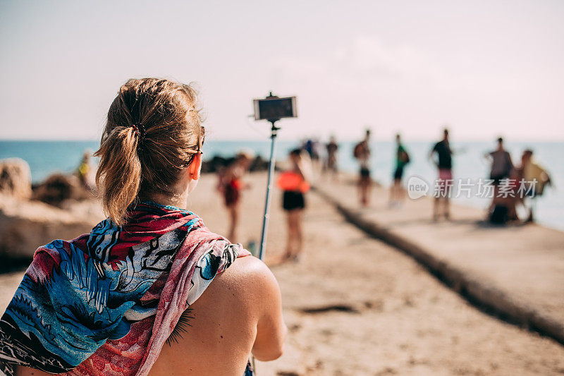 一名年轻女子用手机在码头的自拍杆上拍照