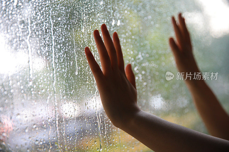 在雨天，年轻女子用手触摸窗户