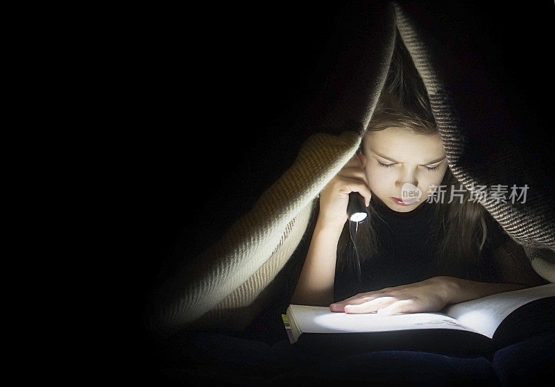 女孩拿着手电筒看书。