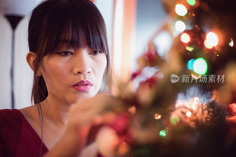 亚洲民族美丽的年轻女子附上圣诞装饰品，装饰圣诞树
