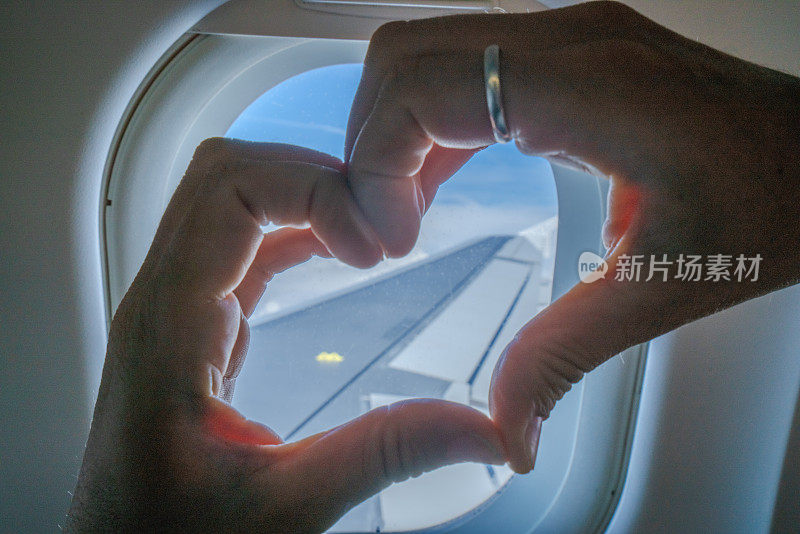 近距离拍摄女性双手在飞机上制作心形指架，用双手热爱旅行和飞行度假的旅游理念