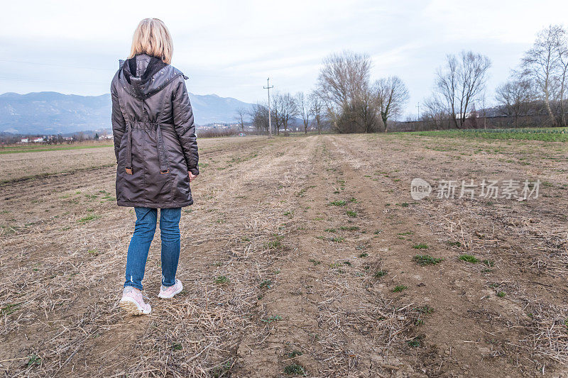 妇女在冬季农田行走的后视图