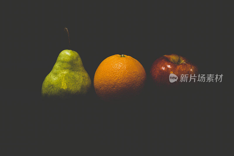 黑色背景下的梨、苹果和橙色水果
