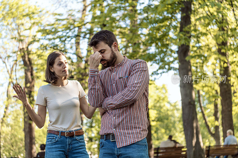 一对年轻夫妇在公园里吵架。年轻夫妇有一个夏天的一天争吵。站在公园外面，困惑的年轻女子打着手势，看着她的男朋友