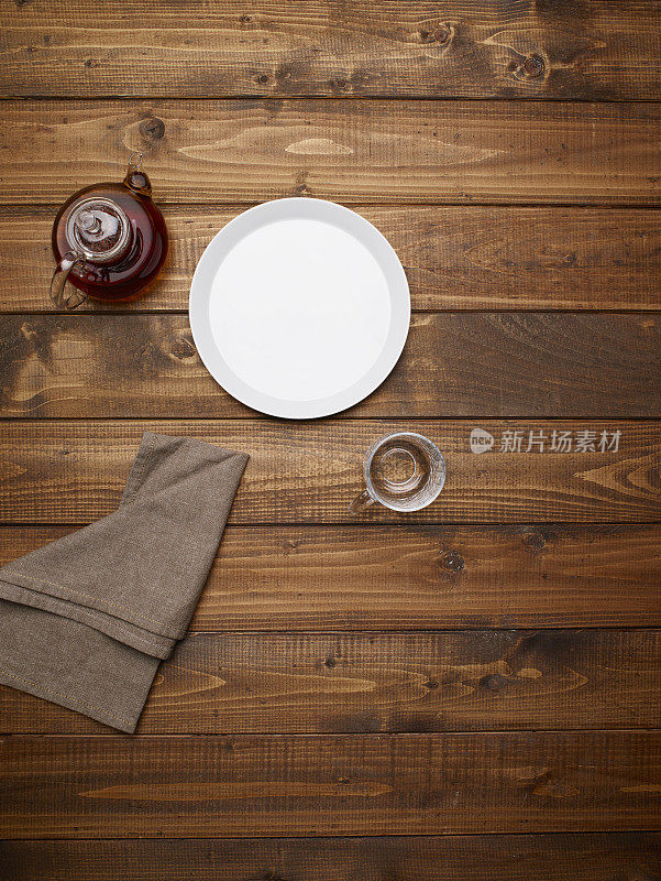 木桌上放置空盘子，茶壶，水杯和餐巾