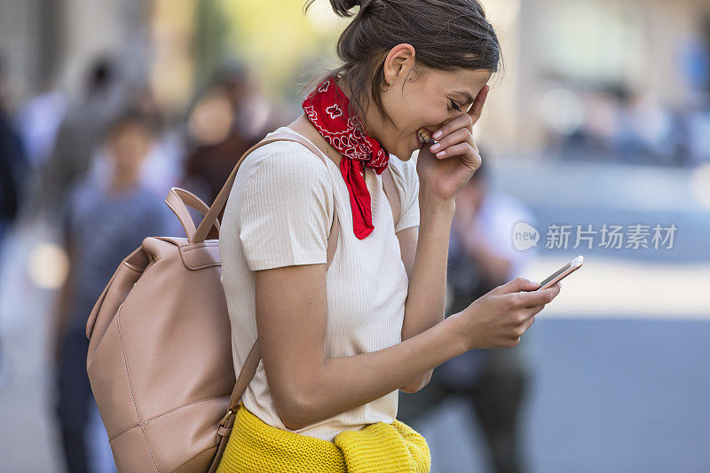 一名年轻女子正带着她的智能手机走在城市的路上