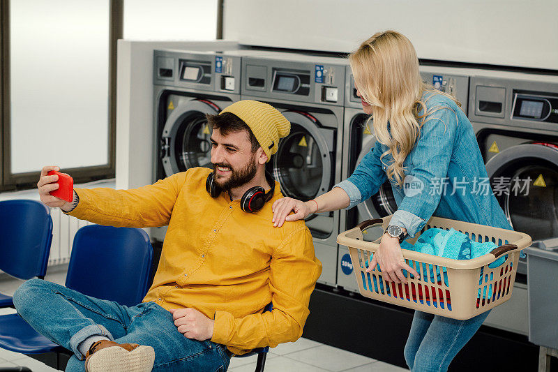 一对快乐的年轻夫妇在洗衣店一起洗衣服。