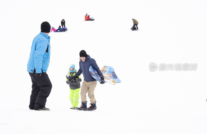 两名男子帮助小孩爬上雪橇山