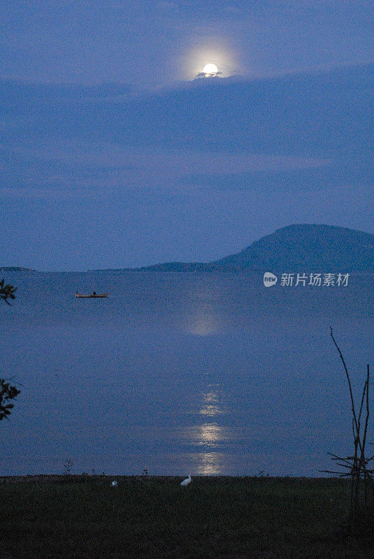传统渔船在一个非洲湖泊上与戏剧性的天空和满月的倒影