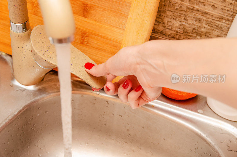 女人棕色的手打开水龙头，厨房特写，水流从水龙头中流出;注意手臂和起重机