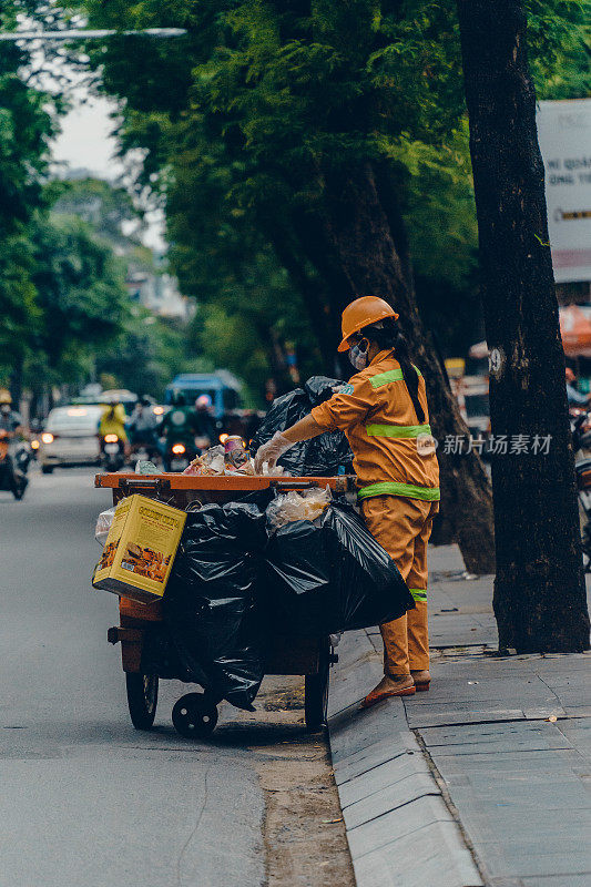 西贡(胡志明市)的街道，俯视图一名女环卫工人推着一辆垃圾车在路上