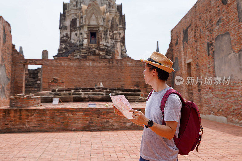 在泰国大城府历史公园的传统寺庙内，一名戴着帽子的年轻亚洲男子正在看地图