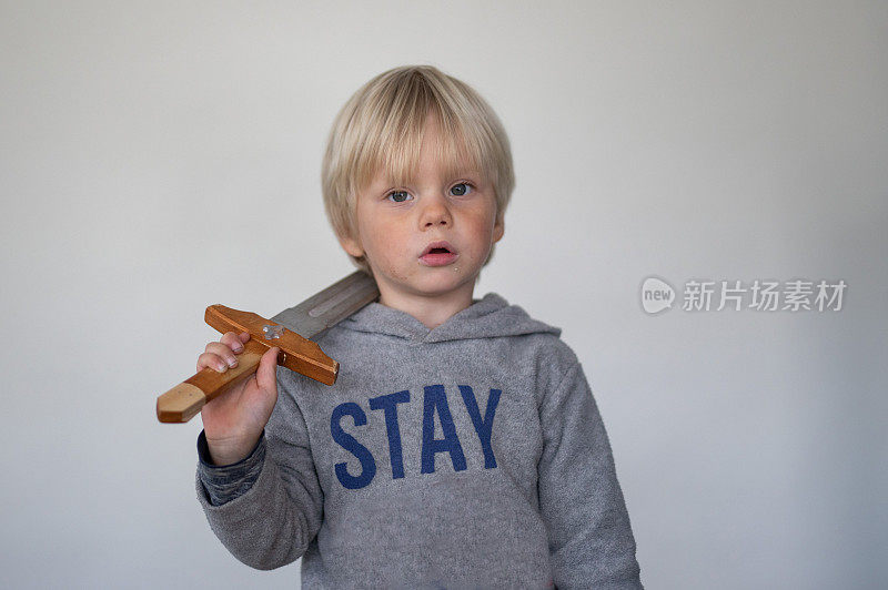 一个小男孩在白色屏幕前摆姿势玩木剑。