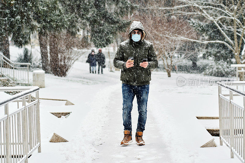 在下雪天，戴着保护面罩和太阳镜的男子在公园里使用手机