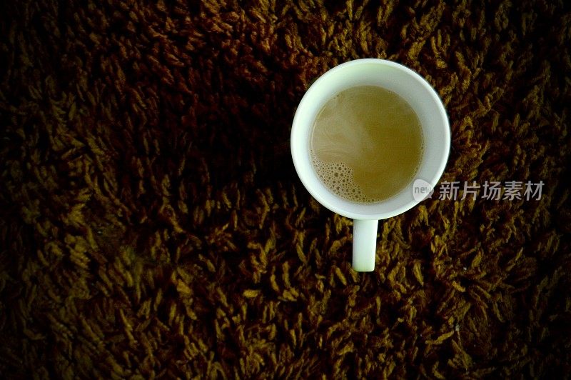 在棕色地毯上，用白色杯子盛一杯热印度茶