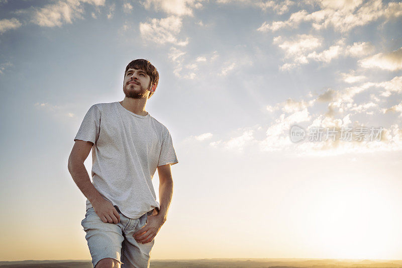 夕阳西下时，一个年轻人站在山顶眺望地平线。想象未来。