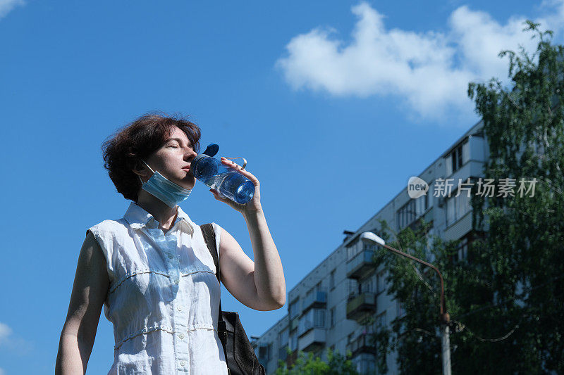 一个成熟的女人在炎热的夏天在城市的街道上喝水