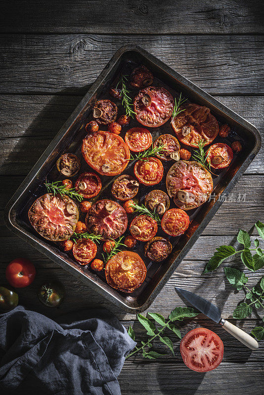 烤番茄切成各种形状，放在烤盘里，木桌上放罗勒和迷迭香