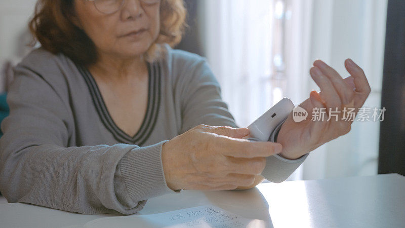 女性手戴腕部监视器，检查血压，并在笔记本上记录血压数字