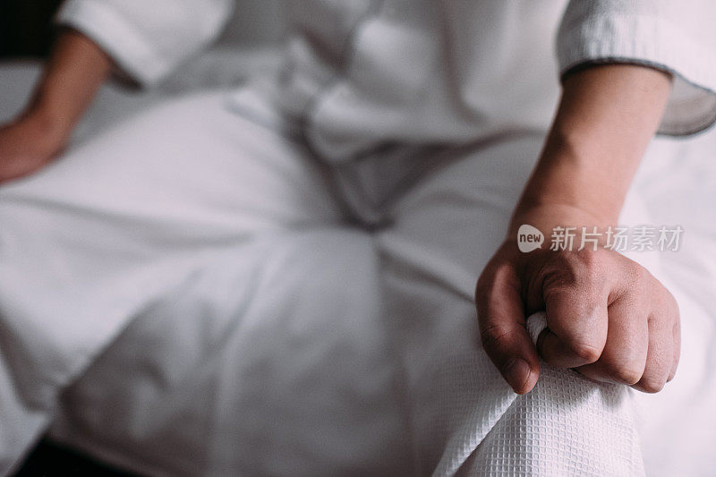 一个男人坐在床上，双手放在膝盖上