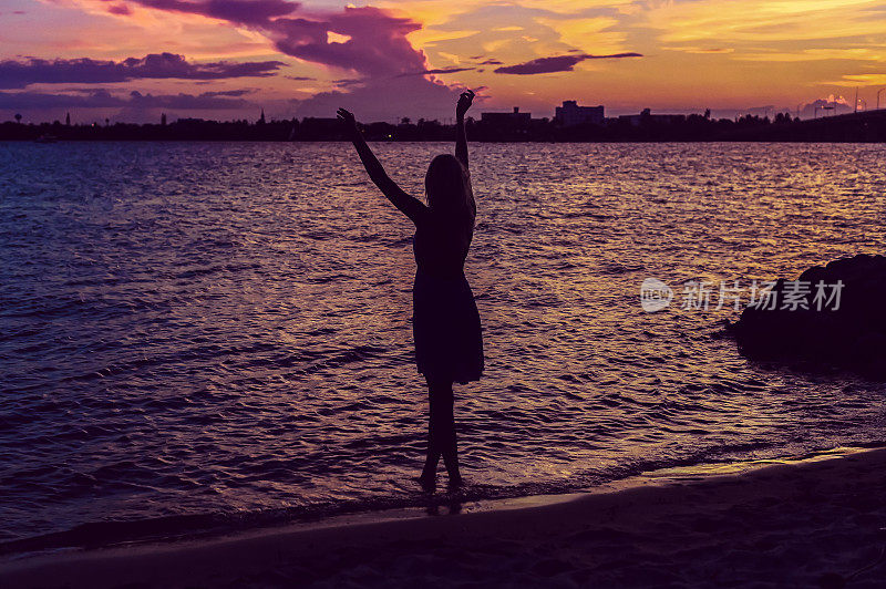在田园式的日落海滩上，一名女子举起双臂