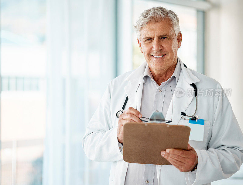 自信成熟的男性医生在医院或诊所阅读剪贴板上的病人记录。一个穿着白大褂的快乐白人老头。在医疗保健领域工作的受信任的医生和从业人员