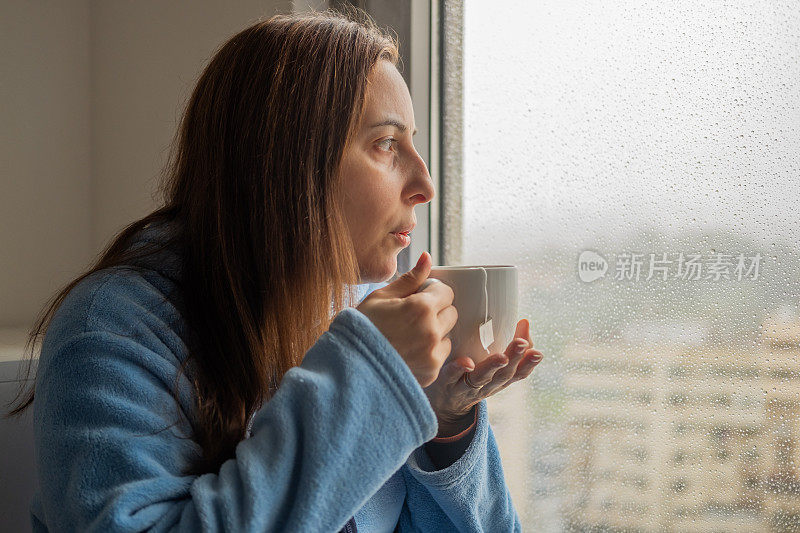 窗外下着雨，女人在窗前喝茶