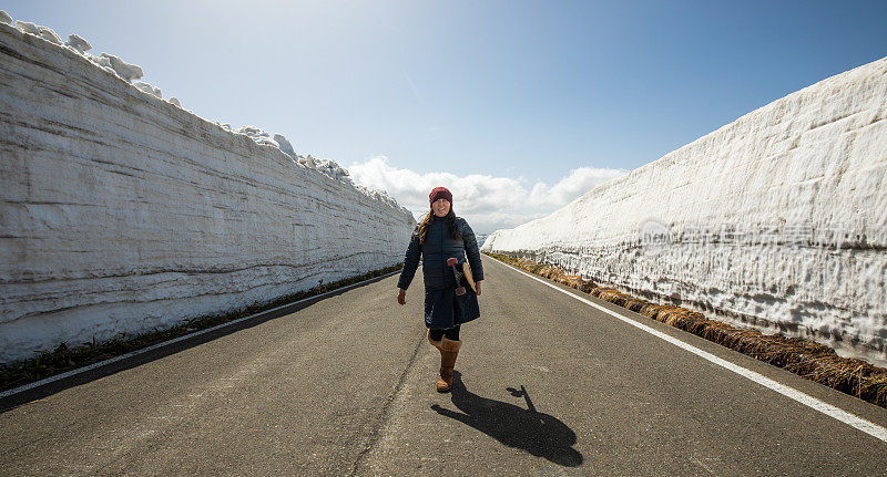 女滑板沿着高高的雪墙的山路行走