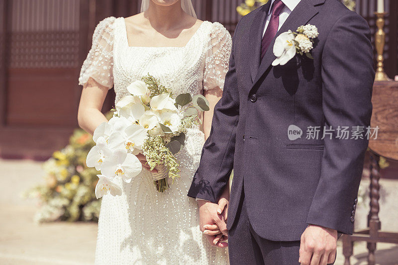 婚礼新人新娘和新郎手牵着手，新娘手里拿着一束花