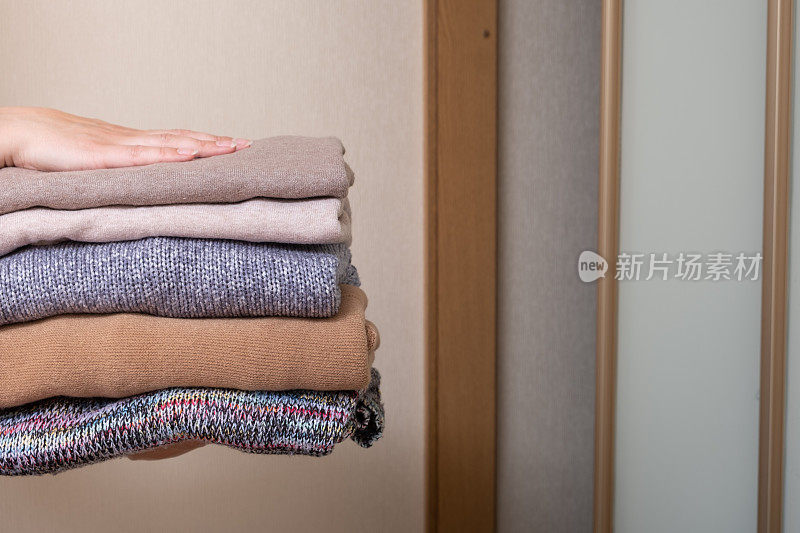 堆叠舒适的针织毛衣在女性的手在门衣柜的背景。温暖的概念