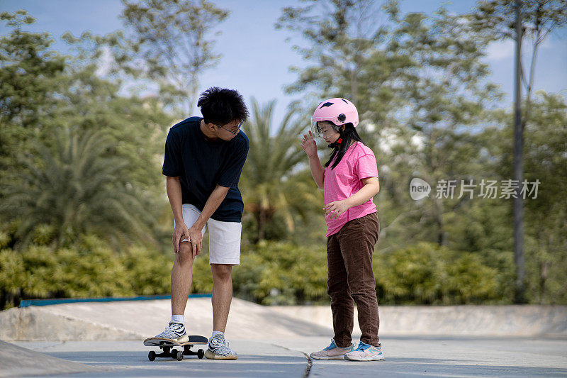 亚洲华裔少年在滑板公园教妹妹玩滑板