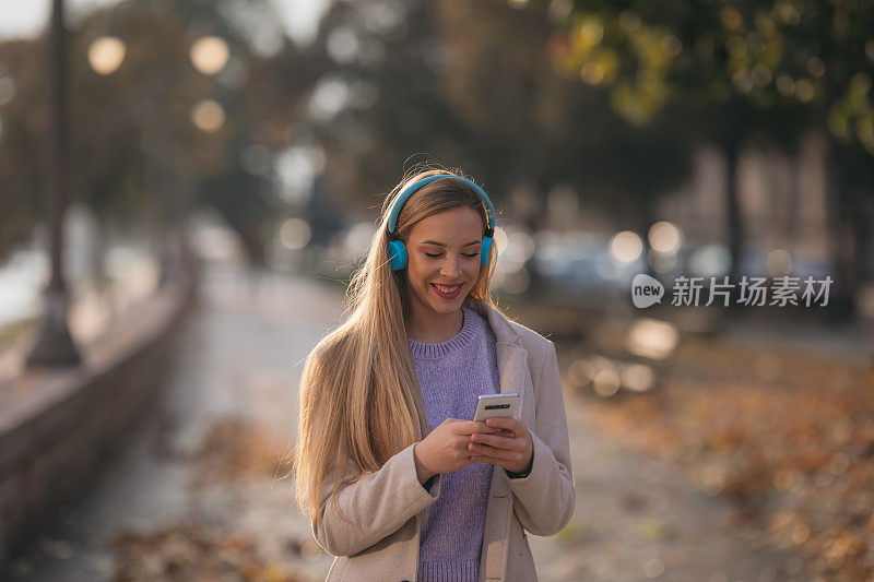 年轻的白人女子在城市里用智能手机和耳机笑得很开心